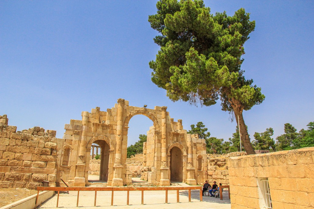 Guida alla visita di Jerash porta dell'antica città romana con albero e persone all'ombra