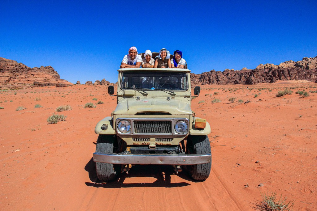 sabbia rossa e colline rocciose del deserto giordano con jeep e 4 persone sopra