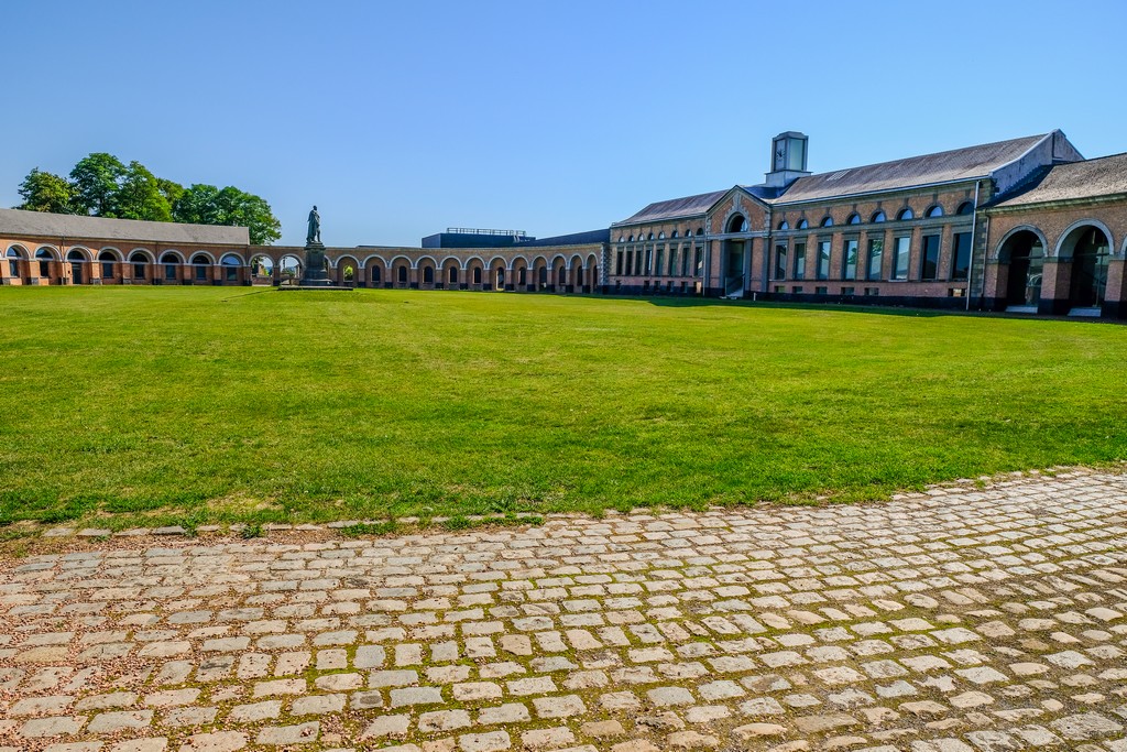 piazza ovale con prato statua al centro ed edifici sui lati con arcate