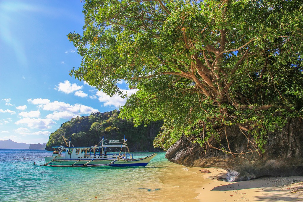 vista di una barca filippina bangka dalla spiaggia con albero