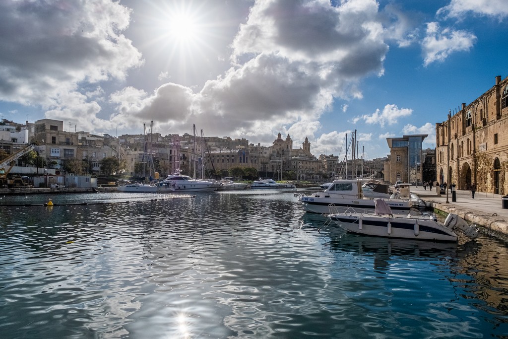 sole si specchia sul porto con barche