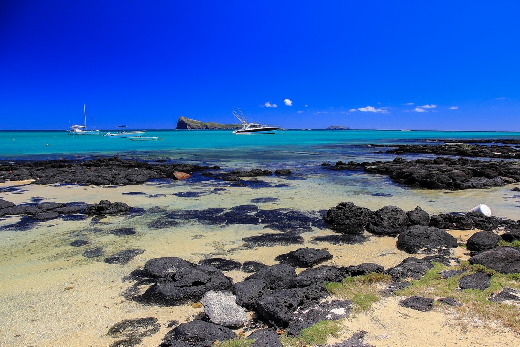 spiaggia con massi neri barche e isole in lontananza