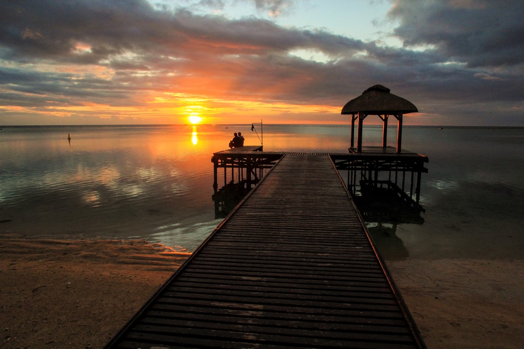 tramonto sul mare con pontile e persone sedute