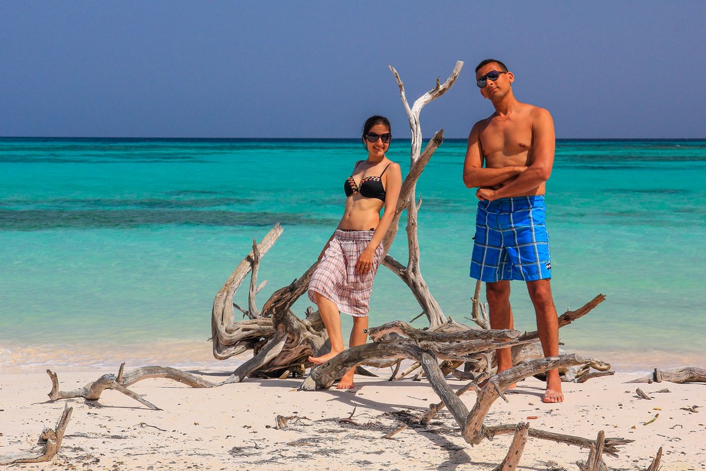 coppia in spiaggia di sabbia bianca con mare turchese e alberi secchi