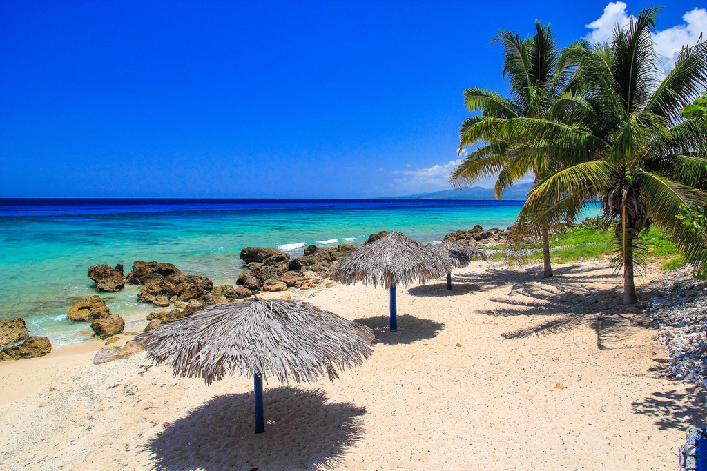 spiaggia di sabbia bianca con mare turchese ombrelloni di paglia e palme