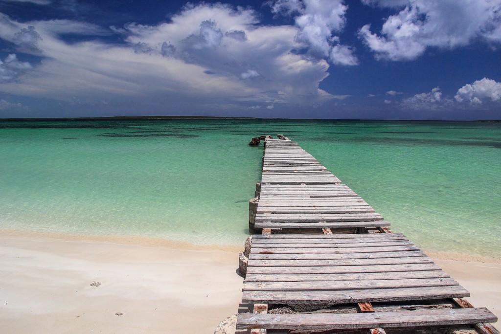 pontile antico di legno si protende verso spiaggia di sabbia bianca con mare turchese