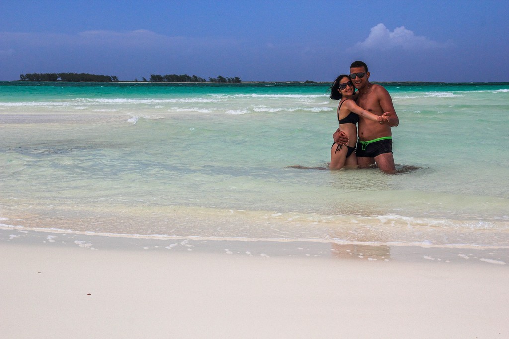 coppia in spiaggia di sabbia bianca con mare turchese con isola dietro