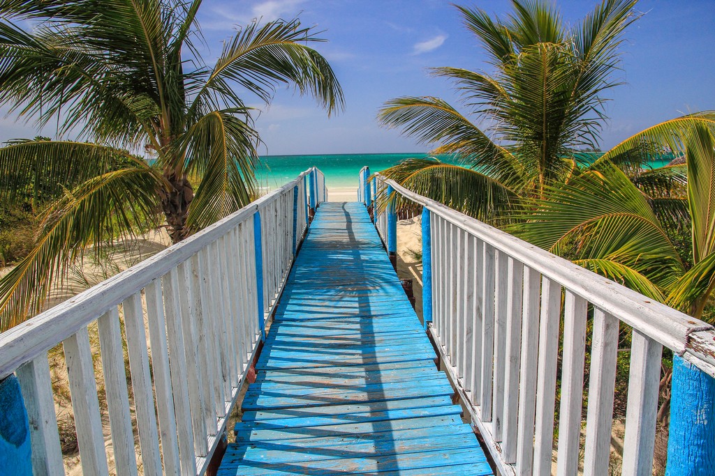 passerella azzurra e palme verso spiaggia di sabbia bianca con mare turchese