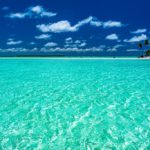 Mare turchese con spiaggia e palme in lontananza cielo azzurro e nuvolette bianche